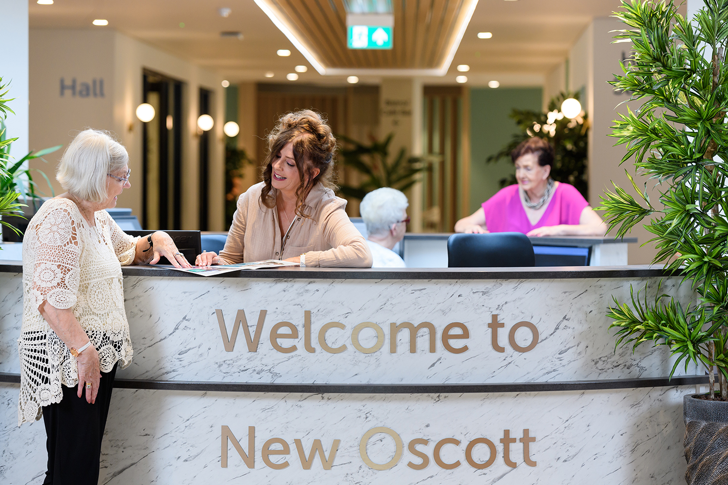 Reception says welcome to New Oscott, a receptionist smiles and chats to a resident.