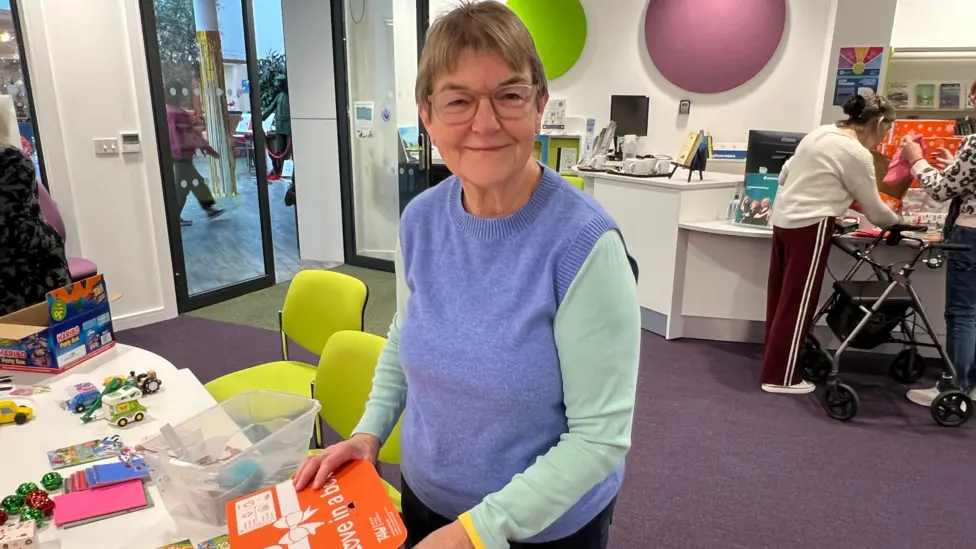 A woman smiles at the camera with a box in her hand.